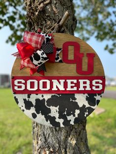 a wooden sign with the word u on it hanging from a tree in front of a grassy field