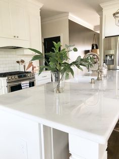 a large white kitchen with marble counter tops and an island in front of the stove