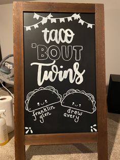 a chalkboard sign with taco bout twins written on it in front of a pile of toilet paper