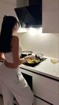 a woman standing in front of a stove with food on top of it next to a glass of wine