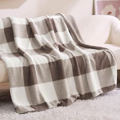 a white couch with a brown and white blanket on it's back next to a chair