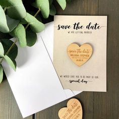 save the date card with wooden heart magnets next to greenery and white envelope