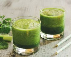 two glasses filled with green smoothie on top of a wooden table