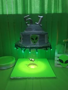 an alien themed birthday cake on a table with green lights and decorations around the cake