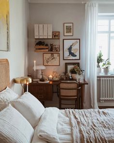 a bedroom with white linens and pictures on the wall above the bed, along with two desks