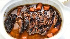 a bowl filled with meat and carrots on top of a white tablecloth covered table