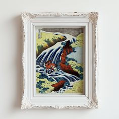 a painting hanging on the wall next to a white framed frame with an image of a waterfall