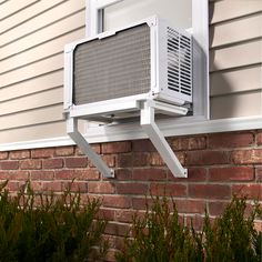 an air conditioner mounted on the side of a brick building next to plants and bushes