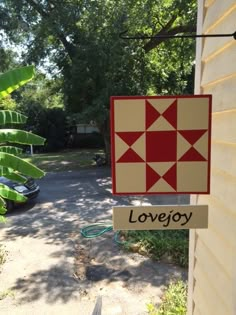 a red and white sign hanging from the side of a house next to a tree