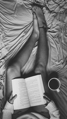 a person laying in bed with an open book and cup of coffee next to them