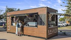 two people are standing outside of a small food stand that is made out of wood