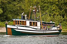 a green and white boat traveling on the water near some trees in front of it