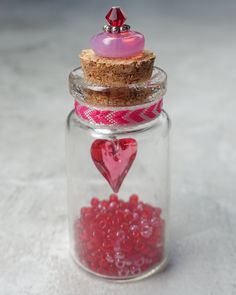 a glass jar filled with red beads and a pink heart shaped object on top of it