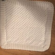 a white knitted blanket sitting on top of a wooden floor