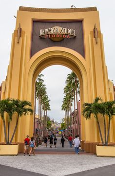 the entrance to universal studios with palm trees and people walking under it on a cloudy day