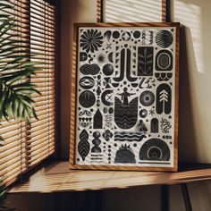 a wooden frame with black and white designs on it next to a window covered in blinds