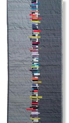 a quilted wall hanging on the side of a gray building with many different colored strips