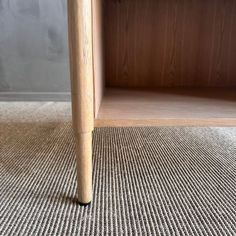 a close up of a wooden shelf on carpeted floor next to a gray wall