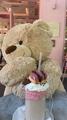 a large teddy bear sitting on top of a table next to a cup filled with donuts