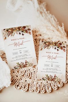 two wedding cards with leaves on them sitting next to a pile of blankets and pillows