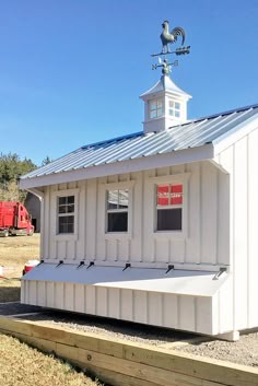 a small white building with a weather vane on it's roof and some windows