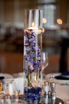 a tall glass vase filled with purple flowers on top of a table next to candles