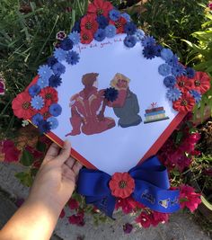 someone holding up a card with an image of two people on it and flowers around them