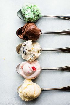 five scoops of ice cream lined up in a row with spoons next to them