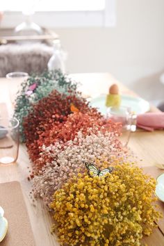 the table is covered with different colored flowers and place settings for dinner guests to sit at