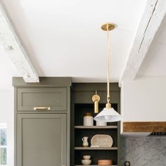 a kitchen with green cabinets and marble counter tops, gold accents on the light fixture