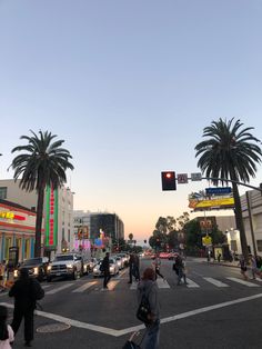 people crossing the street at an intersection with palm trees on both sides and buildings in the background