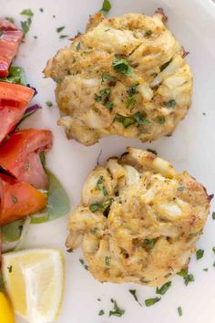 two crab cakes on a white plate with lemon wedges and watermelon slices