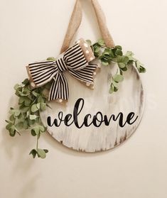 a welcome sign hanging from the side of a white wall with greenery on it