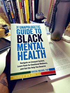 the unapolgetic guide to black mental health is sitting on a desk next to a stack of books