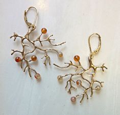 two pairs of gold earrings with corals and pearls hanging from them on a white surface