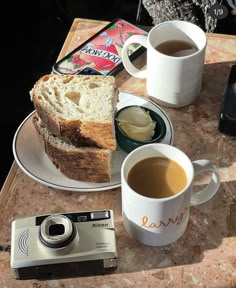 a table topped with two cups of coffee next to a plate of food and a camera