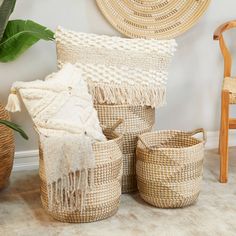 three woven baskets with tassels on the floor next to a chair and potted plant