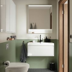 a white toilet sitting next to a bathroom sink under a mirror above a wooden door