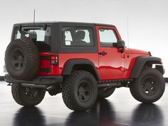 a red jeep is parked in a large room with black tires and rims on it