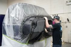 a man in black shirt and hat working on a car with plastic covering it's hood