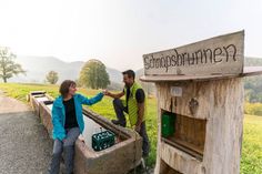 two people shaking hands in front of a wooden structure with writing on it and mountains in the background