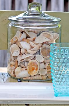 a glass jar filled with seashells sitting on top of a table next to two glasses