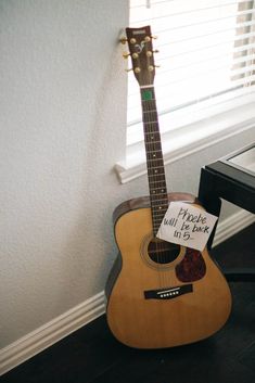 an acoustic guitar sitting on top of a wooden floor next to a window with blinds