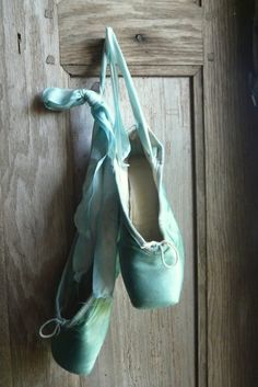 a pair of ballet shoes hanging on a wooden door with a knot tied to it