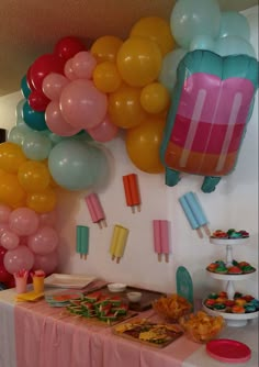 a table topped with lots of balloons next to a wall filled with food and desserts