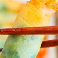 a close up of some food with chopsticks in the foreground and an orange piece of fruit on the other side