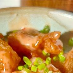 a bowl filled with meat covered in sauce and green onions on top of white rice