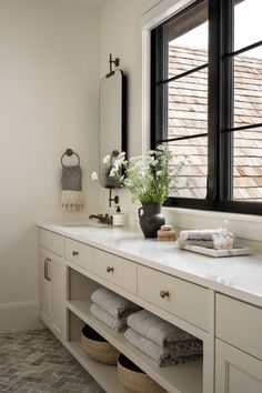 a bathroom with white cabinets and drawers, a large window over the bathtub is filled with flowers