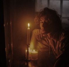 a man sitting in front of a lit candle with his hand on the table next to it