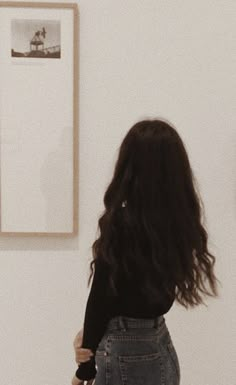 a woman standing in front of a white wall with pictures on the wall behind her